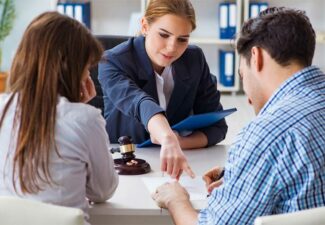 A professional female lawyer in a blue suit discusses documents with a young couple during a consultation in a well-lit office