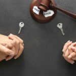 Two pairs of clasped hands, a broken marriage paper, a gavel, and two keys symbolize a divorce agreement