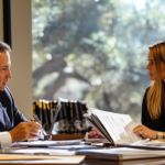 Two divorce attorneys in a professional office, sitting at a large table covered with legal documents and financial statements.