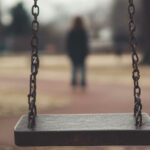Image of an empty swing in a playground, with a distant parent in the background, representing loss of custody due to substance abuse.