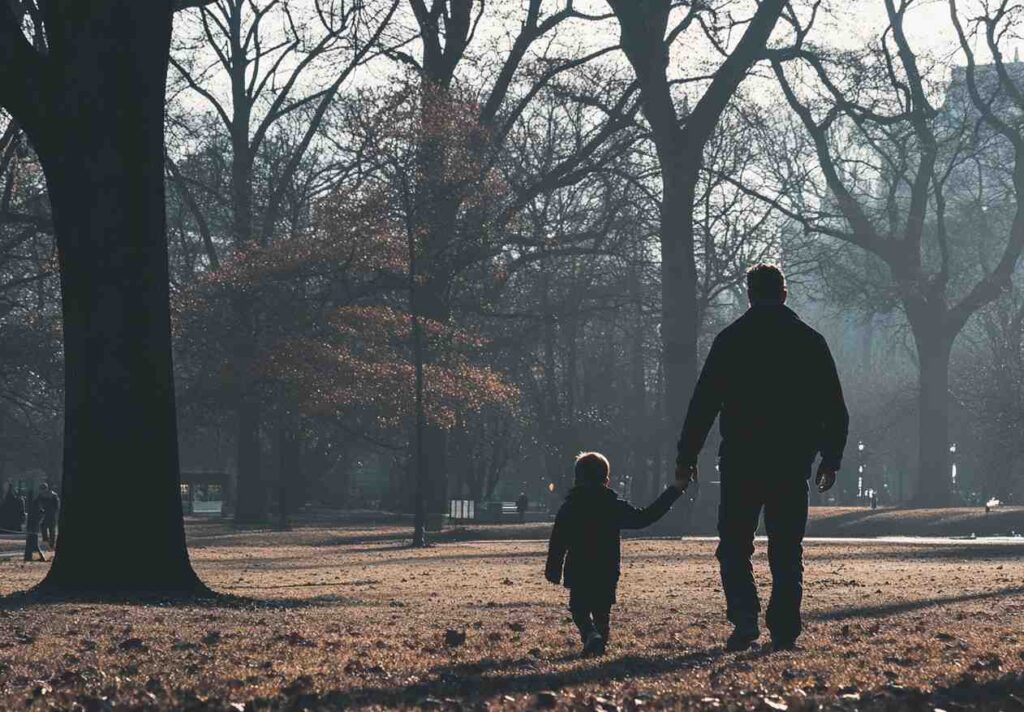 A father and child walking hand in hand in a park.