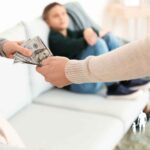 Father handing monetary support to mother with child sitting on a sofa