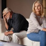 Couple sitting on a couch, appearing upset after an argument in the living room