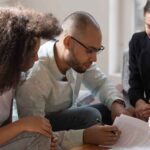 A couple seated at a legal desk, signing a prenuptial agreement with an attorney present.