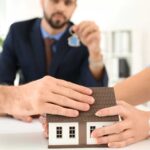 Man and woman each placing a hand on a model house during a legal consultation