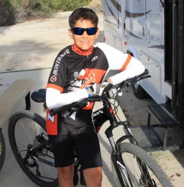 Young male cyclist in black and orange cycling gear with sunglasses leaning on a black mountain bike.