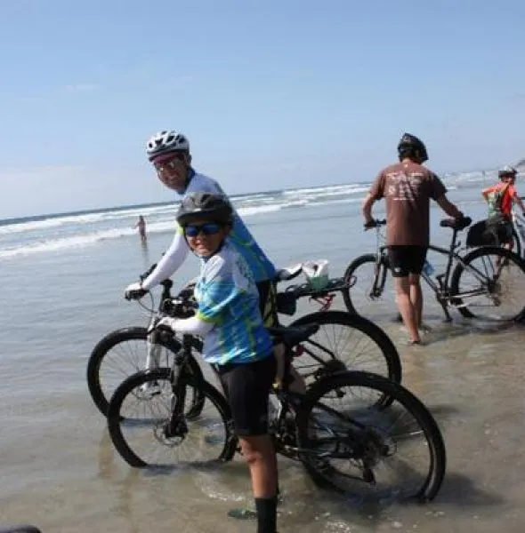 Group of cyclists in helmets standing with bicycles in shallow ocean water under clear sky.