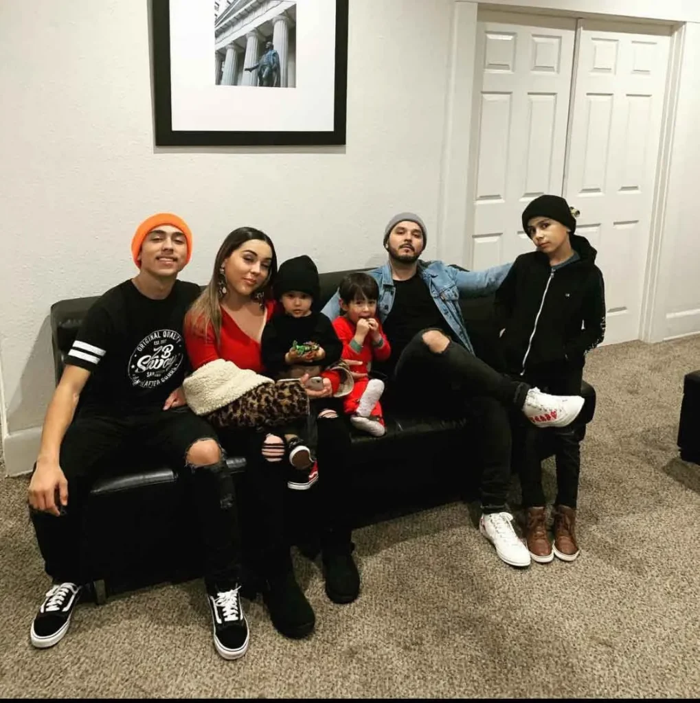Group of six people, including two children, sitting and standing in a living room with neutral decor.