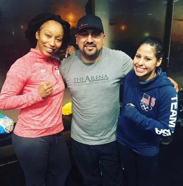 Three people posing indoors, two women in athletic wear and a man in a gray t-shirt and black cap.