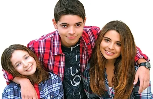 Three smiling teenagers wearing plaid shirts against a white background.