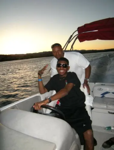 Two men on a motorboat at sunset, one steering and the other standing behind.