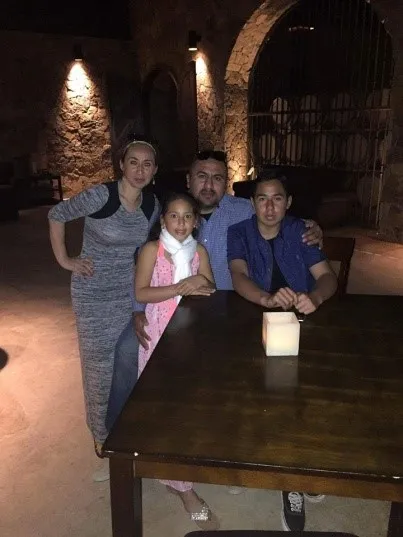Four people posing around a wooden table with a lit candle in a dimly lit stone interior.