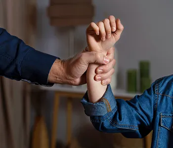 Adult hand firmly gripping child's wrist indoors, both wearing long sleeves.