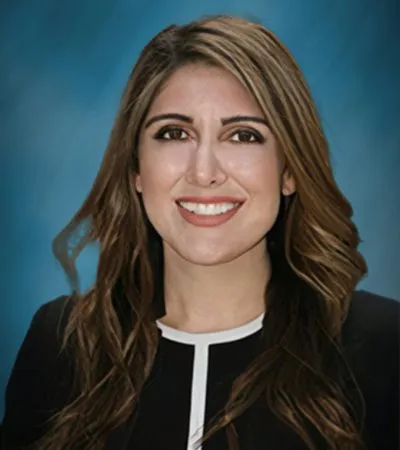 Professional headshot of a smiling woman with long wavy hair against a blue background.