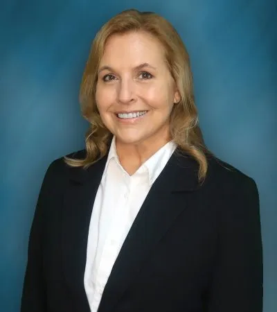 Professional portrait of a smiling woman with blonde hair wearing a black blazer and white shirt.