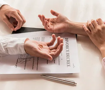 Two individuals holding wedding rings over a divorce decree document on a table.