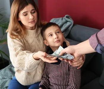 Woman and boy sitting on couch receiving cash from person with extended hand.