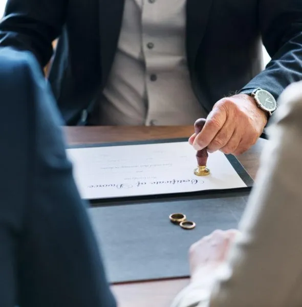 Man in formal attire stamping a marriage certificate on a desk with two gold rings.