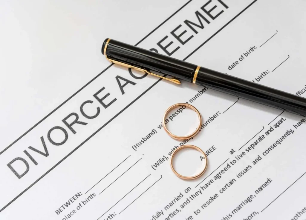 Divorce agreement document with two gold rings and a black pen on white paper.