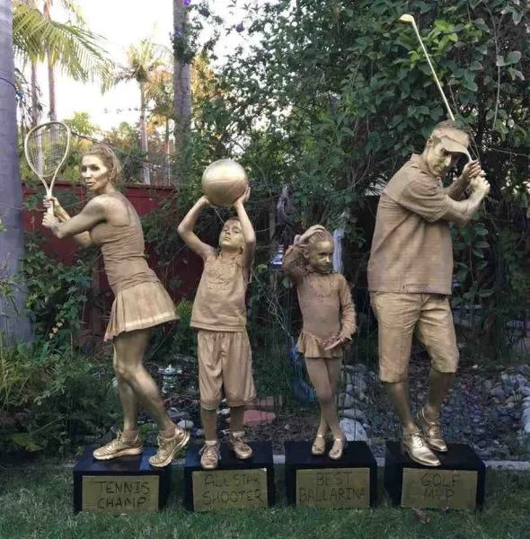 Four people painted gold posing as sports statues labeled Tennis Champ, All-Star Shooter, Best Ballerina, and Golf Champ.