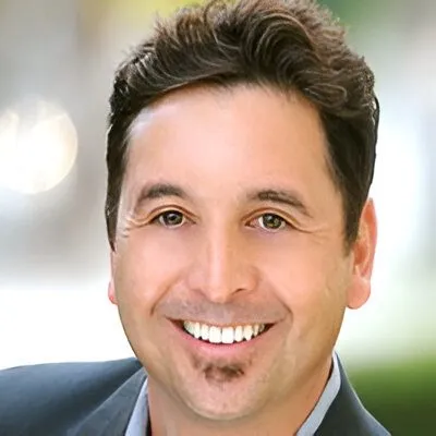 Headshot of a smiling man with dark hair and a trimmed goatee, wearing a suit jacket.