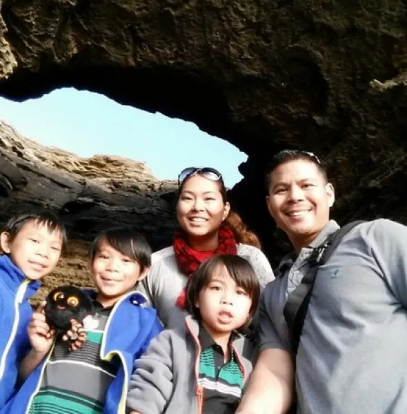 Family of five posing inside a rocky cave opening with natural light.