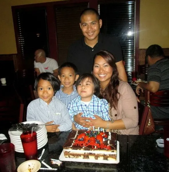 Family of five posing behind a decorated birthday cake with red and black frosting.