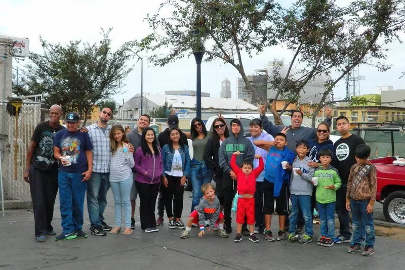 Group of diverse adults and children posing outdoors on a city street with trees and buildings in the background.
