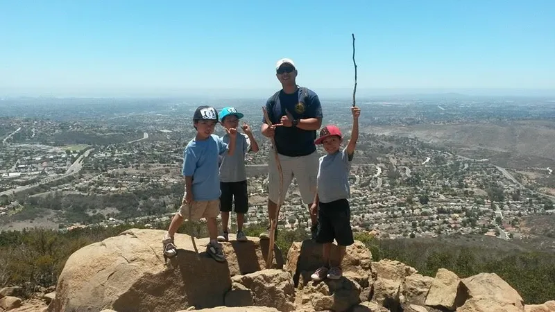 Group of one adult and three children standing on rocky hilltop with cityscape in background.