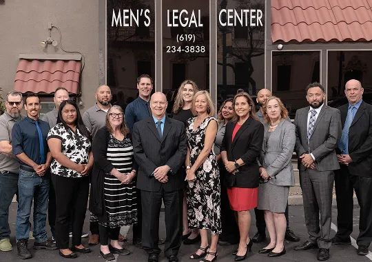 Group of professionally dressed men and women standing outside Men's Legal Center with visible signage and phone number.