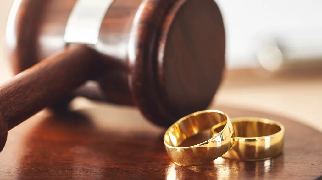 Close-up of two gold wedding rings beside a wooden judge's gavel on a table.