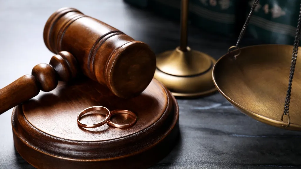 Wooden judge's gavel and base with two wedding rings, and brass balance scale.