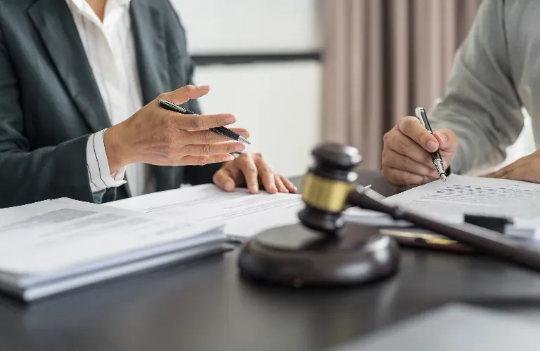Two professionals reviewing legal documents at a desk with a wooden gavel in the foreground.