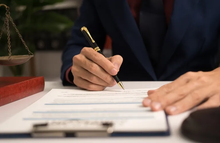 Close-up of a person in a dark suit signing a document with a black and gold pen.