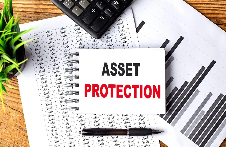 Notepad with "Asset Protection" text, calculator, pen, financial documents