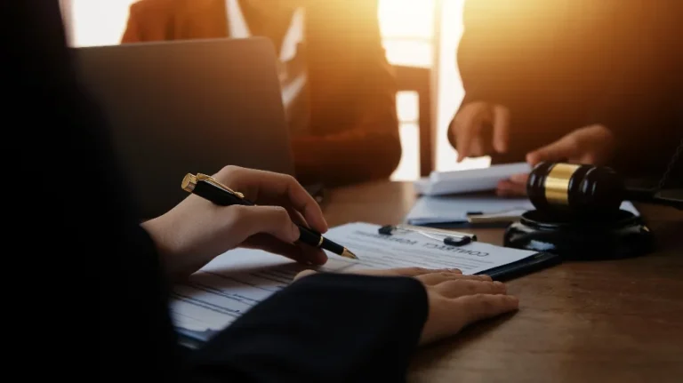 Person signing a legal contract on a clipboard with a judge's gavel on the table.