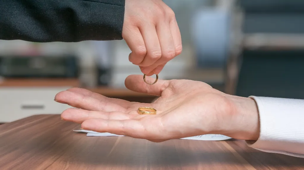 Two hands exchanging gold rings over a wooden table with blurred background.