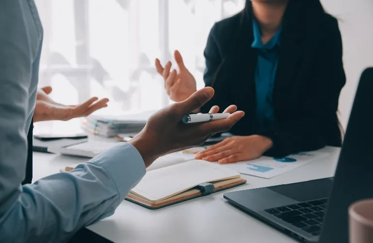 Two professionals engaged in a discussion at a desk with documents and a laptop.