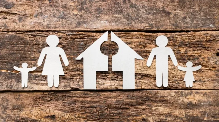 White paper cutouts of a family and a house on a textured wooden background.