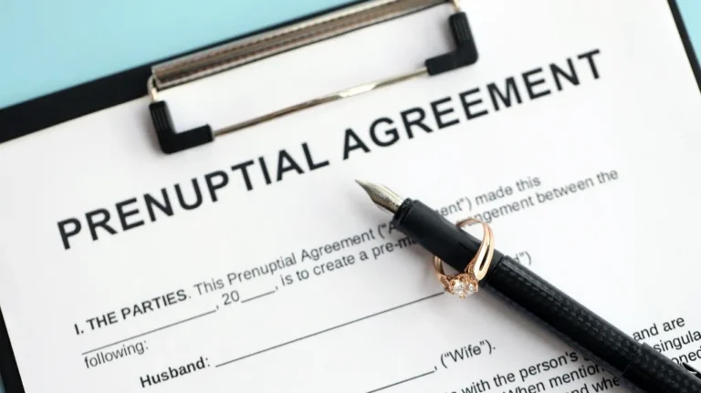 Black pen with a gold ring placed on a prenuptial agreement document on clipboard.