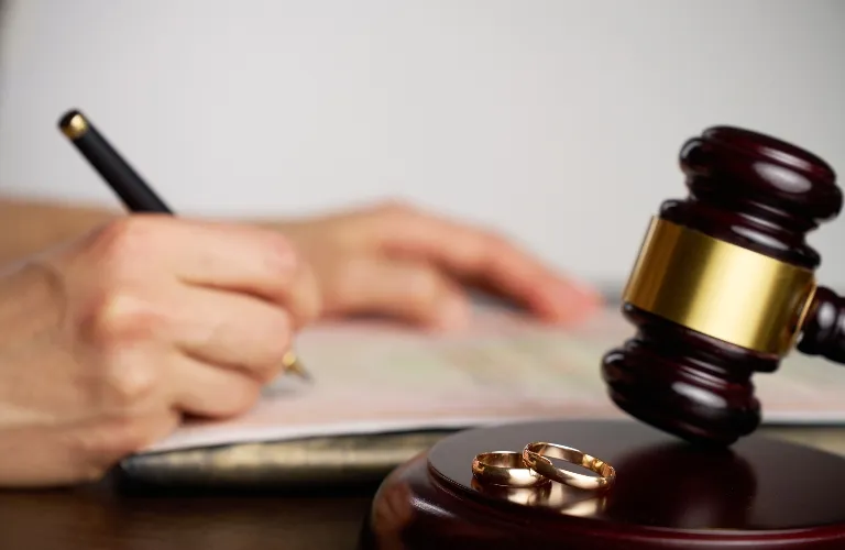 Close-up of wedding rings on judge's gavel with person signing document in background.