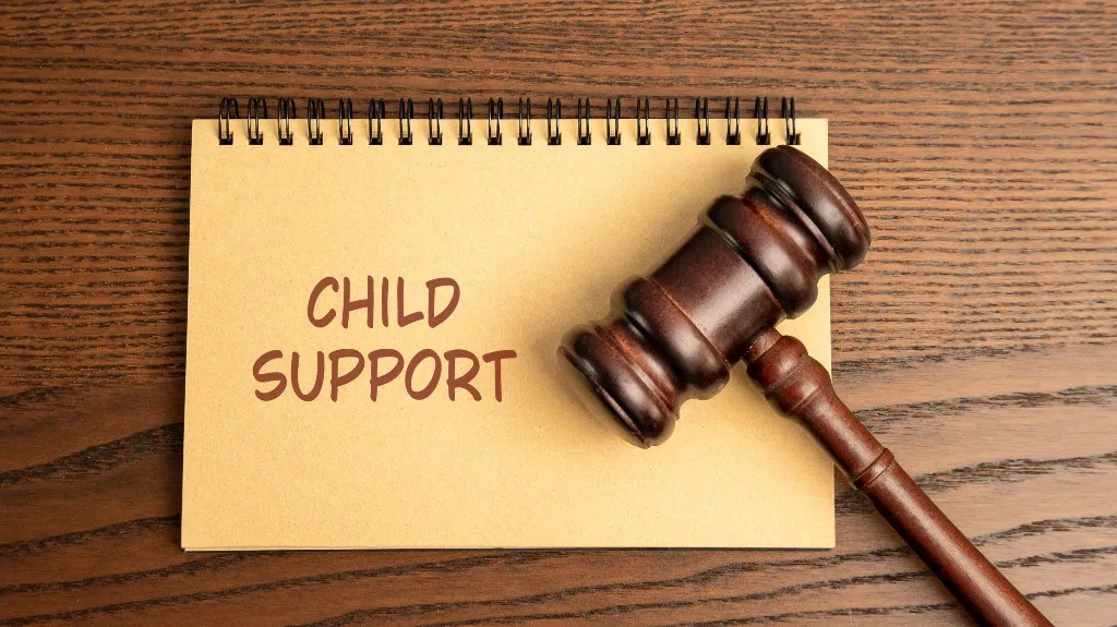 Spiral notebook with "CHILD SUPPORT" text and a wooden judge's gavel on a wood surface.