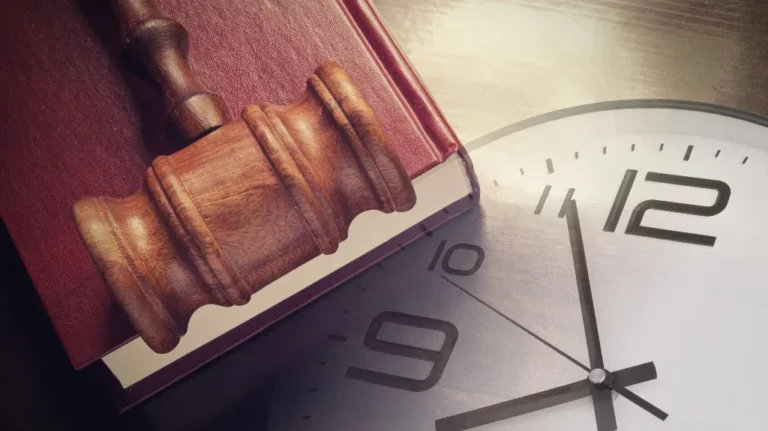 Wooden judge's gavel resting on a red law book beside a large clock face.