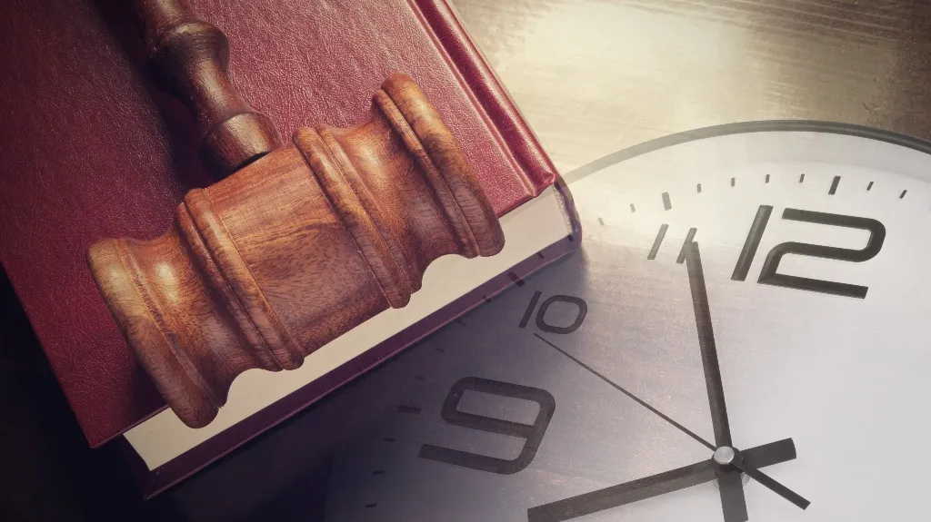 Wooden judge's gavel resting on a red law book beside a large clock face.