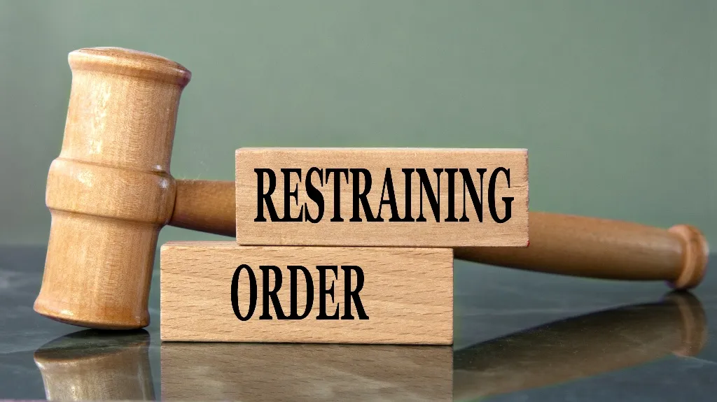 Wooden judge's gavel resting behind two wooden blocks with the text "RESTRAINING ORDER.