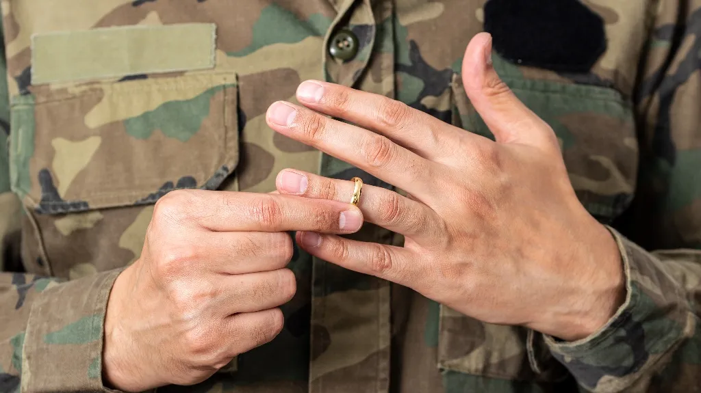 Close-up of a person in camouflage uniform removing a gold ring from their finger.