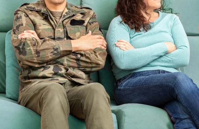 Two people sitting on a teal couch with arms crossed, facing away from each other.