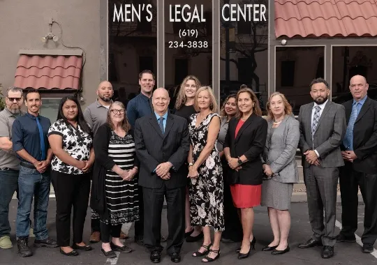 Group of professionally dressed men and women standing outside Men's Legal Center with contact number visible.