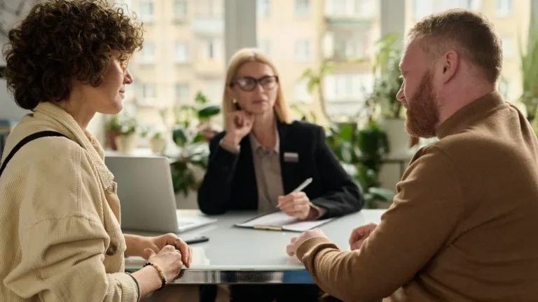 Three professionals engaged in a discussion around a conference table in a bright office.