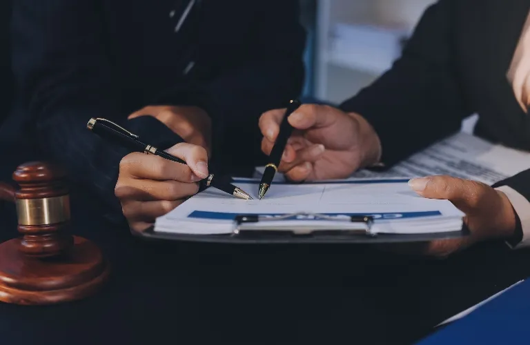 Two individuals in formal attire reviewing and signing documents beside a wooden gavel.